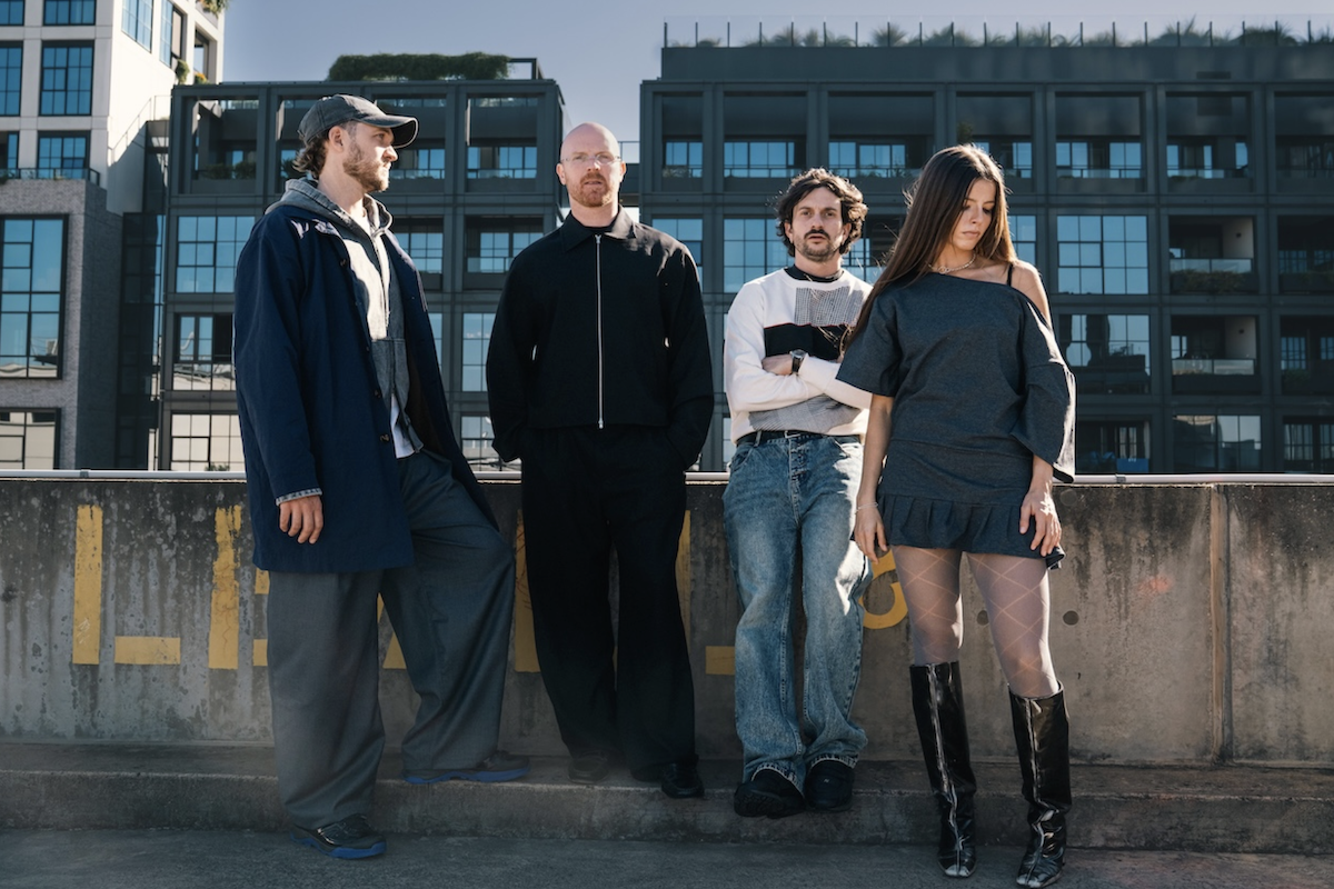 Australian indie rock band The Jungle Giants stand outdoors against modern apartment buildings in stylish streetwear and dark outfits.